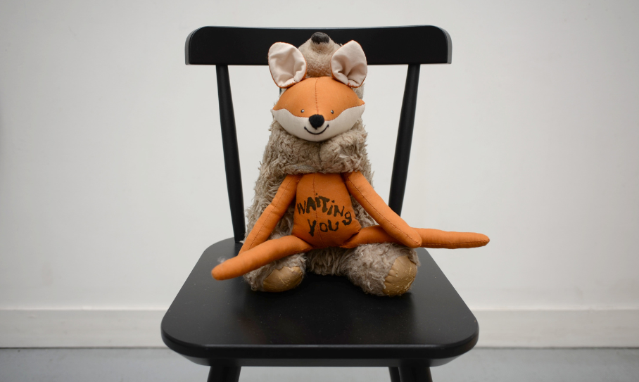 Peluche hybride cousue d'Annette Messager, mi-renard mi-ours, portant l'inscription waiting you, posée sur une chaise noire