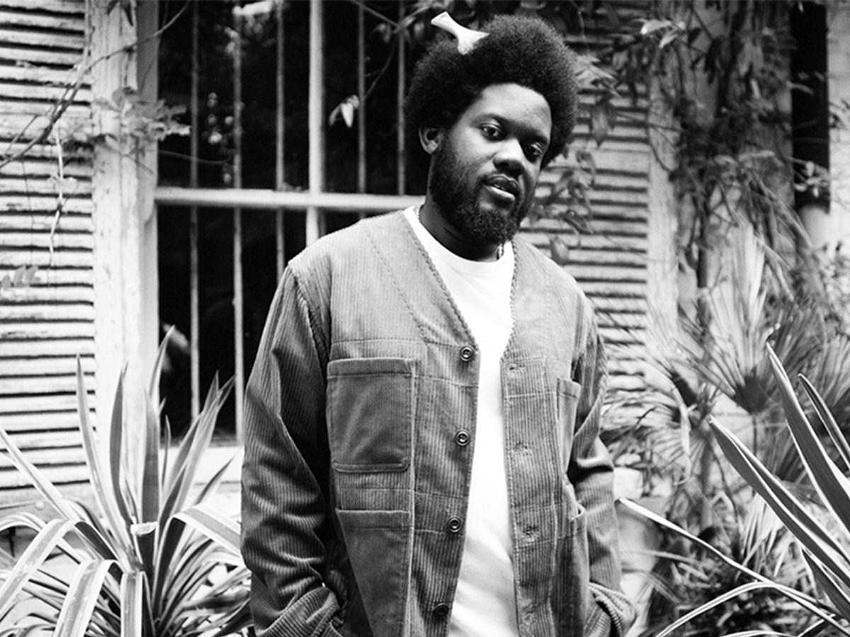 Michael Kiwanuka en veste de velours cotele devant une maison, photo de presse pour l'album Fudge