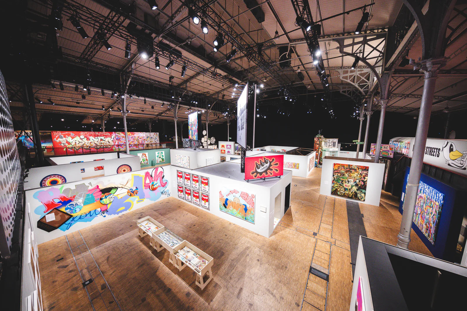 Vue de l'exposition Beyond The Streets sous la charpente de la Grande Halle de La Villette, murs couverts de graffitis colores