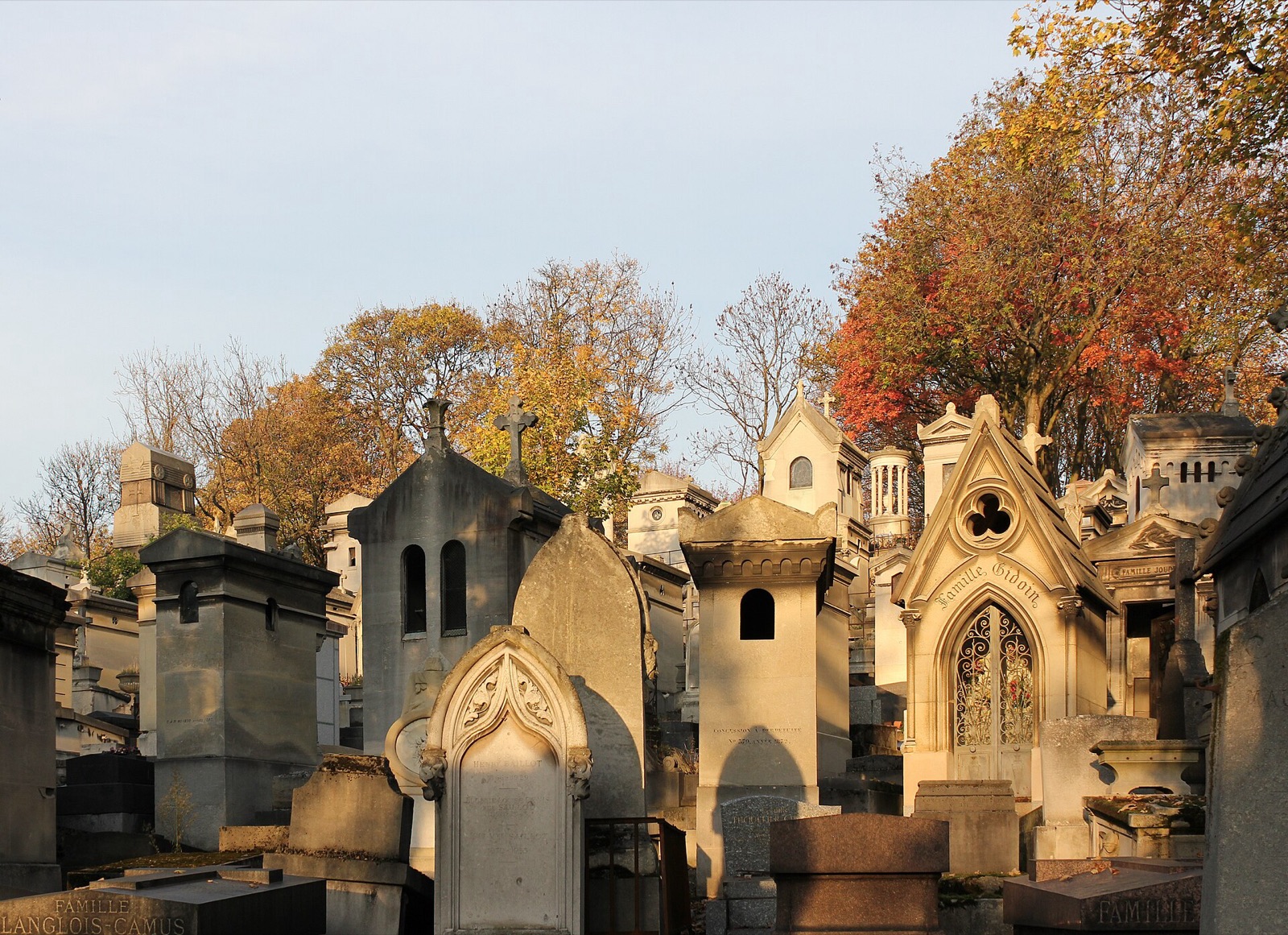 Tombes et chapelles du cimetière du Père-Lachaise à Paris sous la lumière dorée de l'automne, avec des arbres roux en arrière-plan