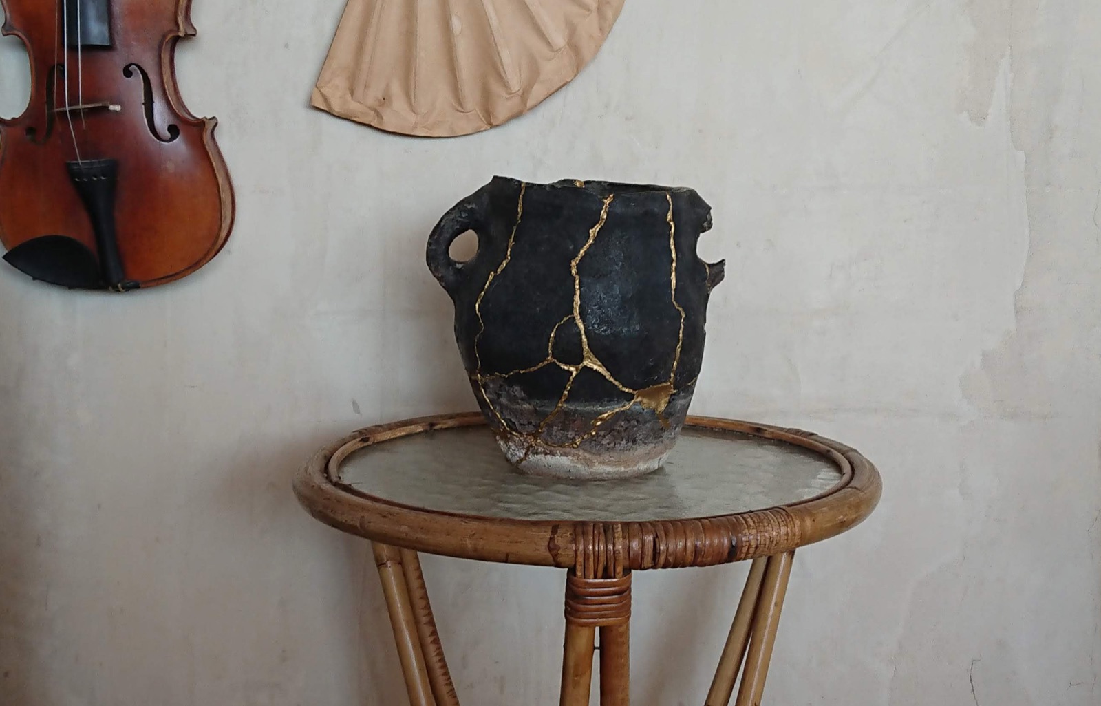 Vase en céramique sombre réparé au kintsugi, avec des veines dorées le long des fêlures, posé sur une table en rotin