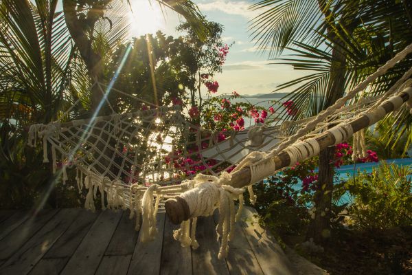 Hamac en corde tendu entre des palmiers au soleil, invitant à la sieste l'après-midi