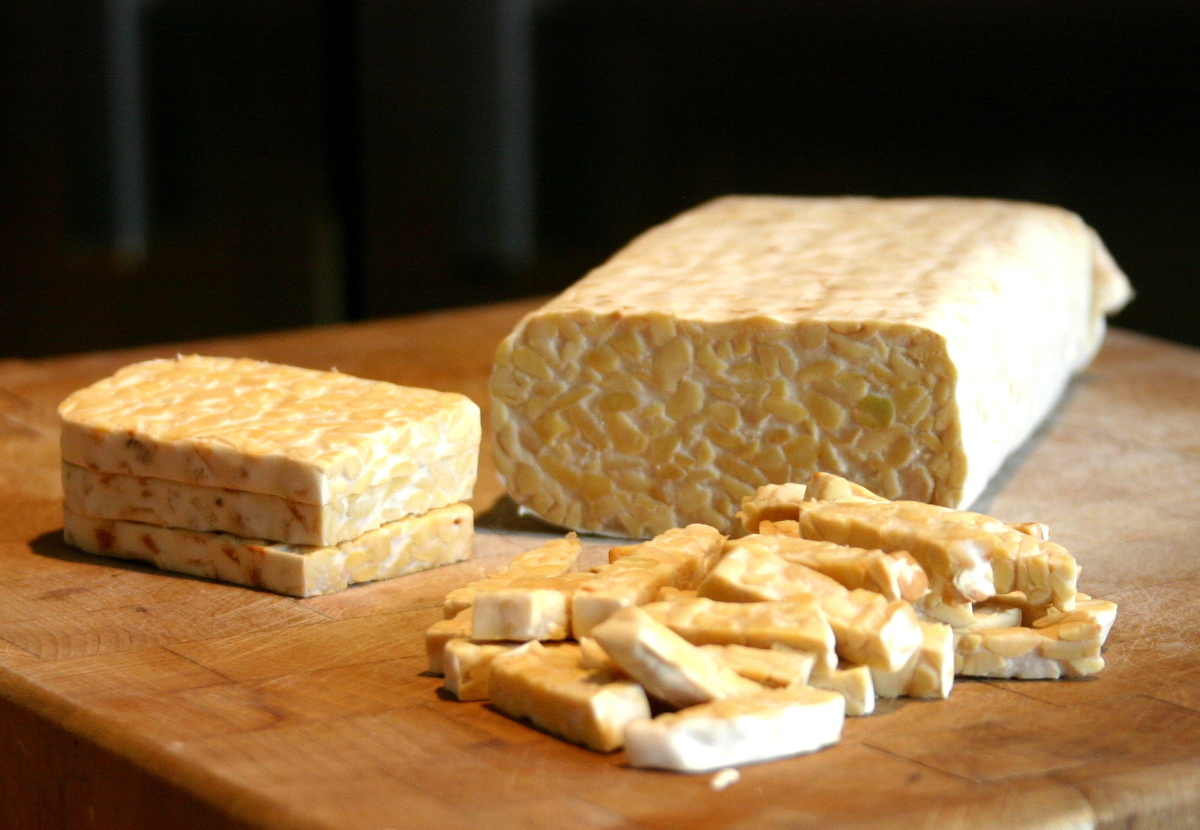 Un pain de tempeh entier et des tranches de tempeh posés sur une planche en bois