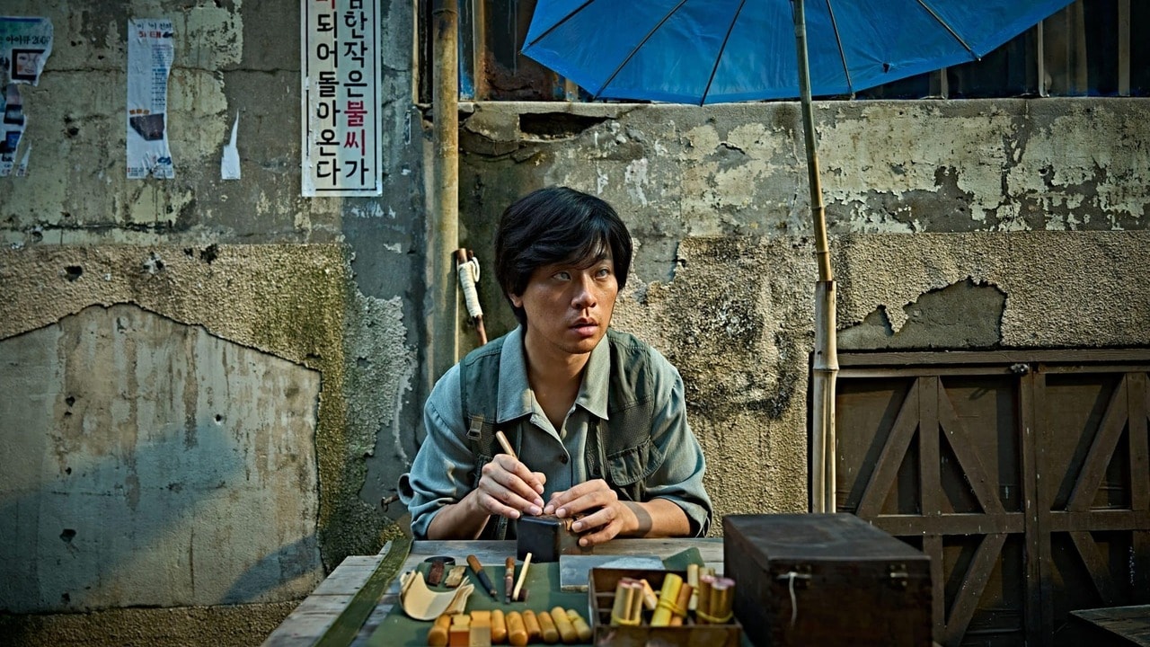 Un artisan grave un sceau à un étal de rue dans la Corée des années 70, scène du film The Ugly de Yeon Sang-ho