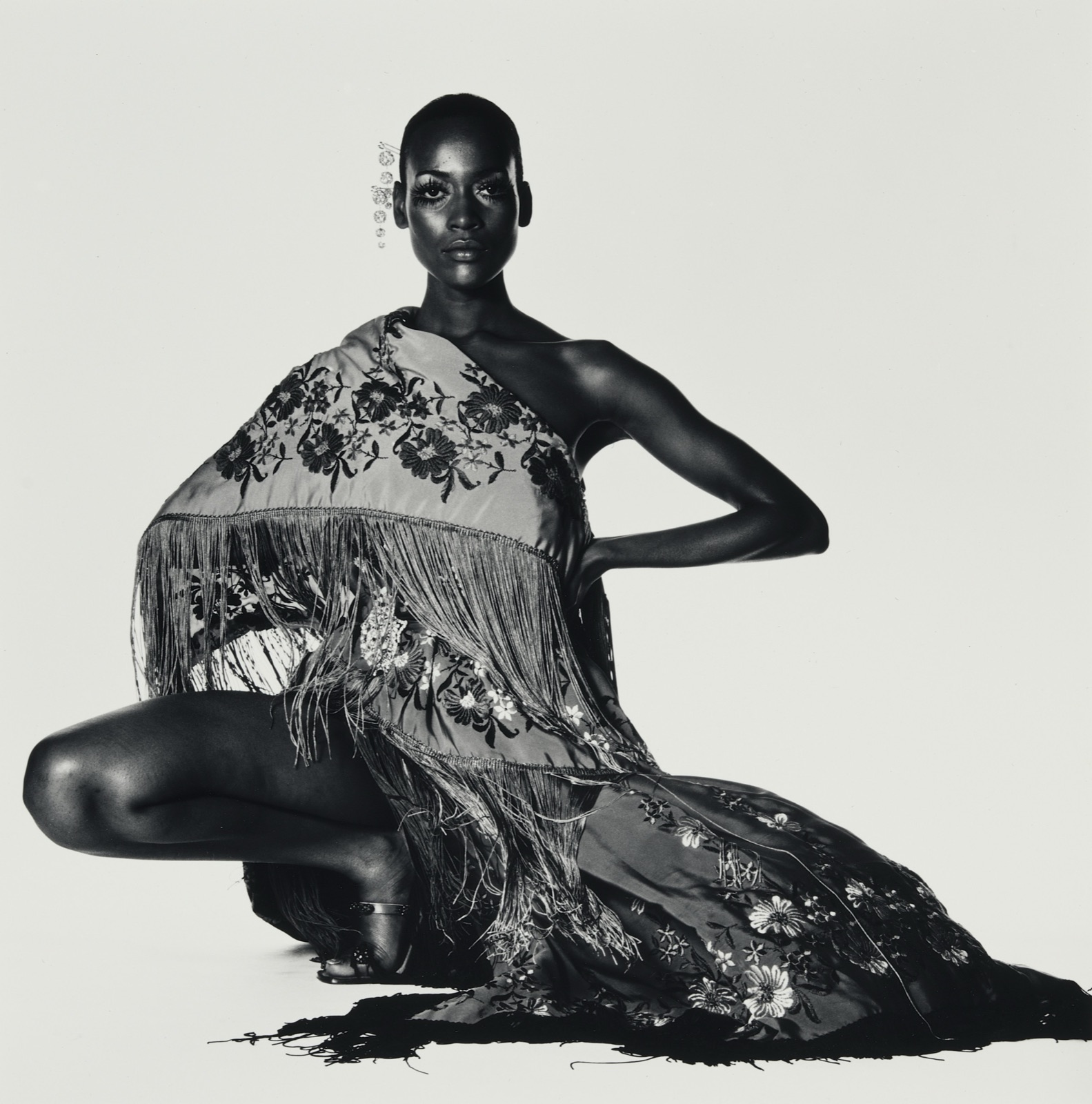 Portrait de mode en noir et blanc signé Irving Penn, modèle assise drapée dans un châle à franges sur fond clair