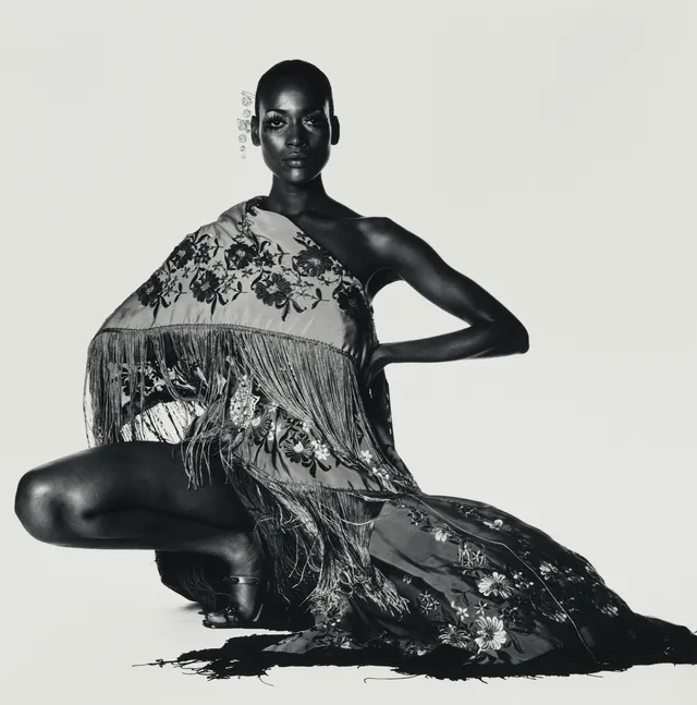 Portrait de mode en noir et blanc signé Irving Penn, modèle assise drapée dans un châle à franges sur fond clair