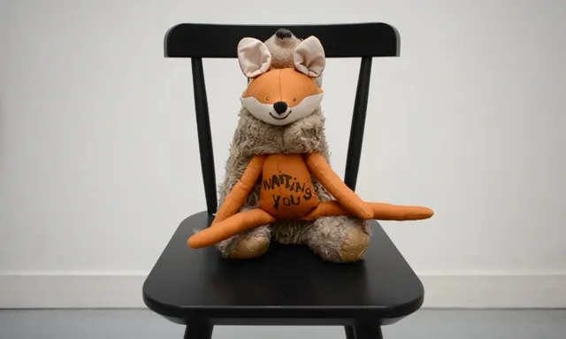 Peluche hybride cousue d'Annette Messager, mi-renard mi-ours, portant l'inscription waiting you, posée sur une chaise noire