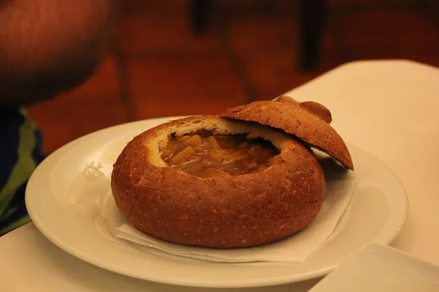 Soupe goulash servie dans une miche de pain évidée, sur une assiette blanche