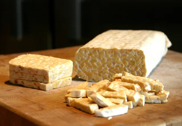Un pain de tempeh entier et des tranches de tempeh posés sur une planche en bois