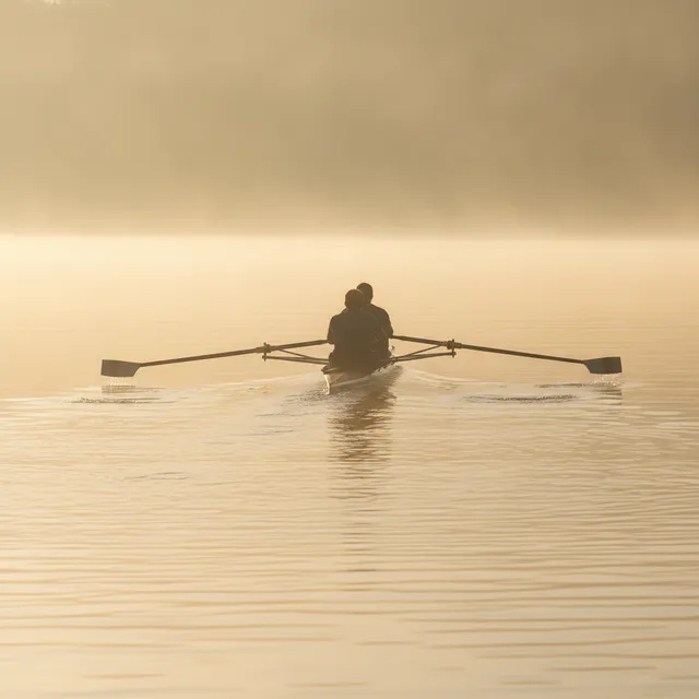 Un aviron de couple glisse sur un plan d'eau calme dans la brume dorée du petit matin
